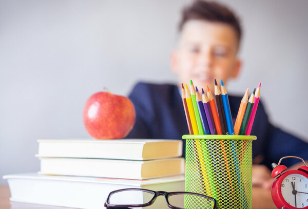 Schreibtisch mit Büchern, Stiften, einem Wecker - im Hintergrund ein Kind